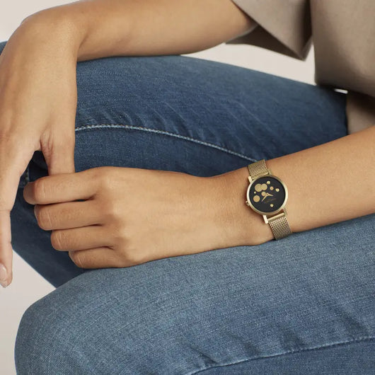 Elegant ladies' wristwatch with paw print design on black dial, placed on model's arm resting on denim fabric.