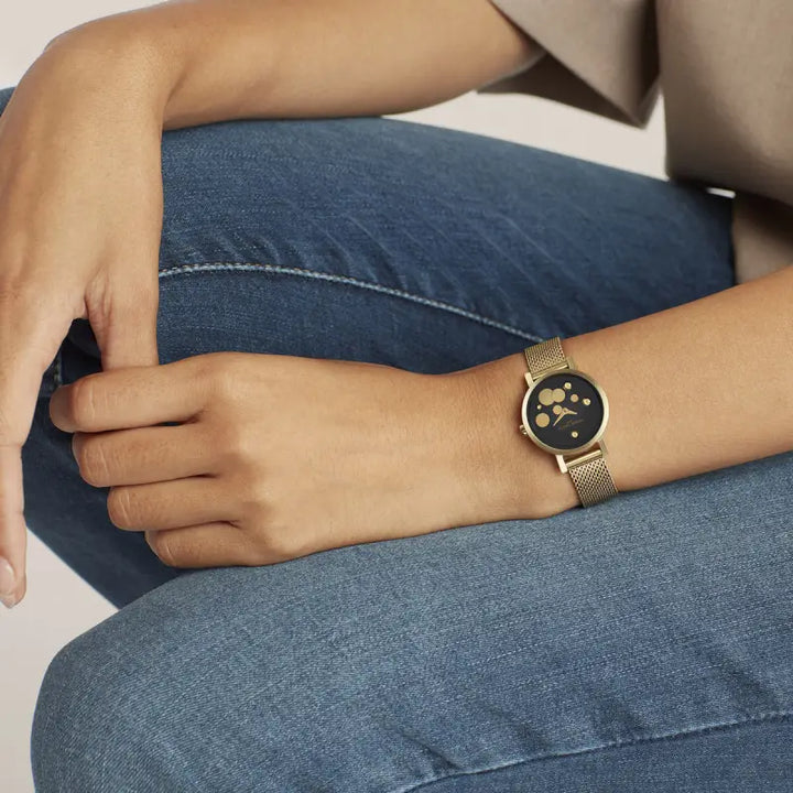 Elegant ladies' wristwatch with paw print design on black dial, placed on model's arm resting on denim fabric.